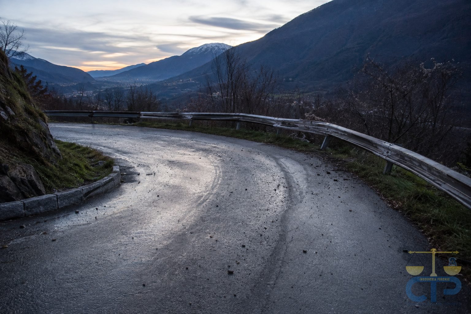 Curva di montagna con tenui strisciate di sbandata sull'asfalto e guard-rail deformato verso l'esterno